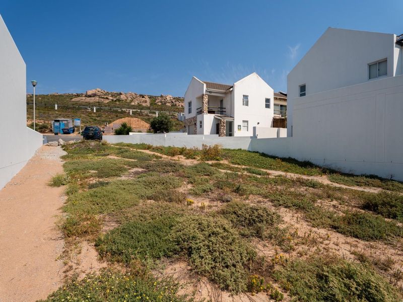 A vacant residential plot featuring sandy ground and native vegetation, enclosed by boundary walls in a developed neighborhood setting.