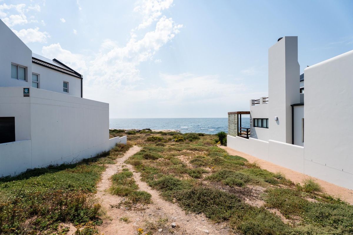 A scenic view of the ocean from a residential plot, featuring a natural pathway between two modern white coastal properties.