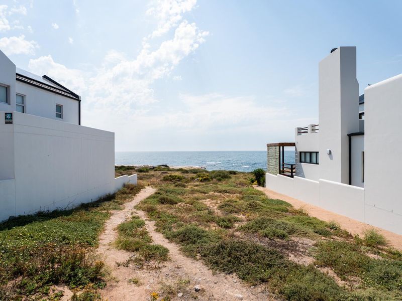 A scenic view of the ocean from a residential plot, featuring a natural pathway between two modern white coastal properties.