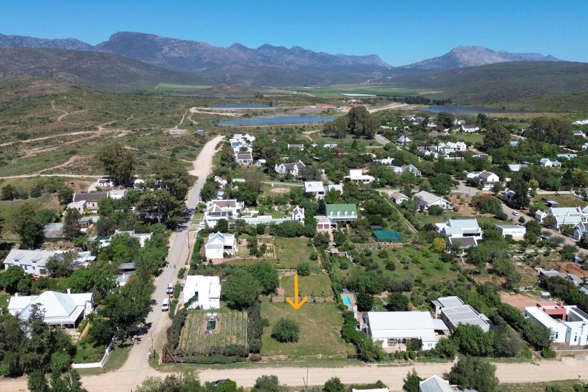 An aerial view of a vacant residential plot situated within a scenic estate, surrounded by established gardens and mountain views.