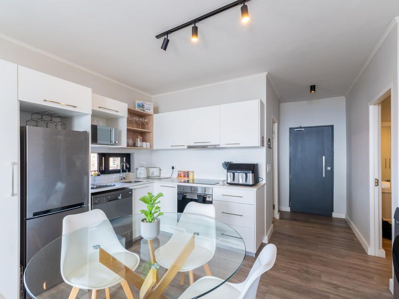 Modern open-plan kitchen featuring white cabinetry, integrated appliances, and track lighting, seamlessly flowing into the living area with durable laminate flooring.