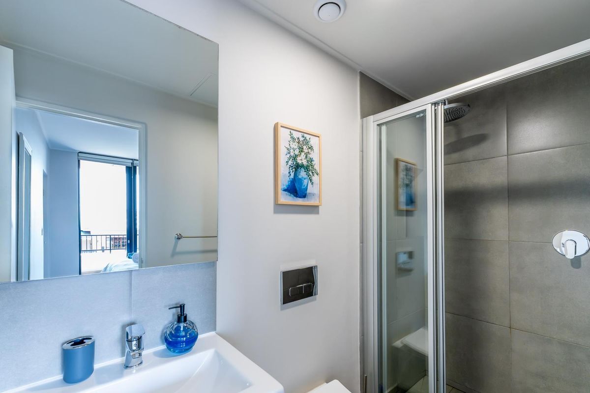 Modern bathroom featuring a vanity basin with mixer tap, wall-mounted mirror, and a glass-enclosed shower with grey tiled walls.