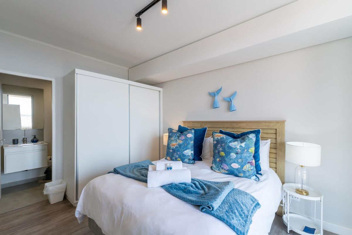 A well-maintained bedroom featuring a built-in wardrobe, modern track lighting, and laminate flooring, with an adjoining en-suite bathroom visible.