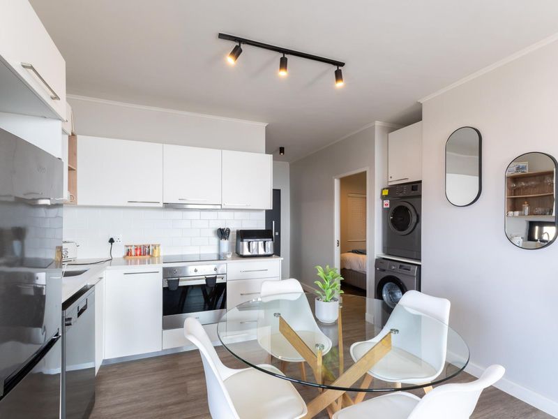 Modern open-plan kitchen and dining area featuring white cabinetry, subway tile backsplash, integrated appliances, and convenient stacked laundry facilities.