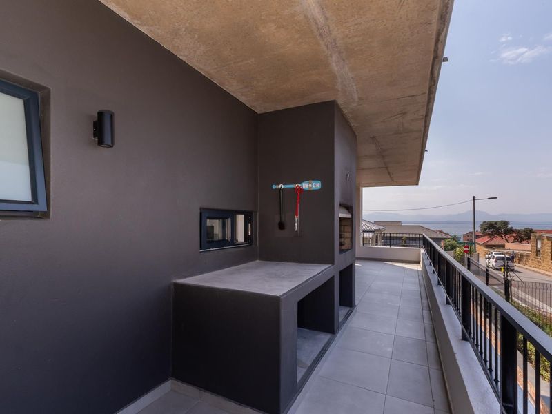 A modern covered balcony featuring a built-in braai, concrete prep area, tiled flooring, and metal railings with views of the surrounding neighborhood.