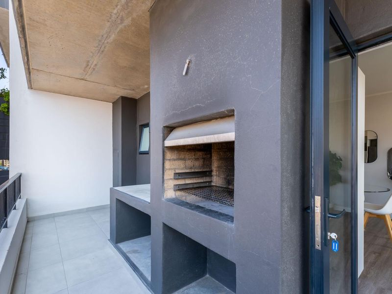 A modern balcony featuring a built-in braai, concrete prep area, and tiled flooring, offering a functional outdoor entertainment space.