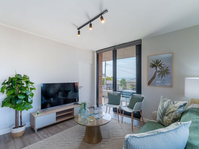 A bright living room featuring modern track lighting, laminate flooring, and a large sliding glass door providing access to the balcony.