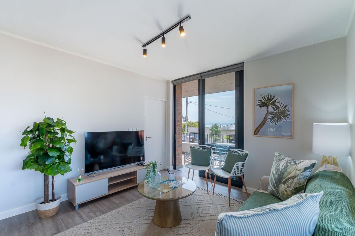 A bright living room featuring modern track lighting, laminate flooring, and a large sliding glass door providing access to the balcony.