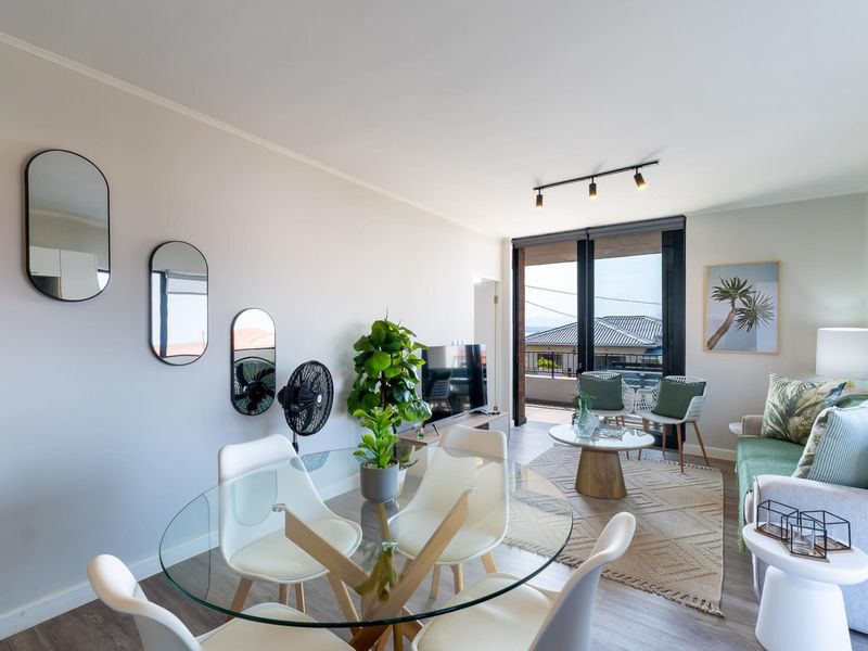 Bright open-plan living and dining area featuring modern track lighting, laminate flooring, and large sliding glass doors leading to a balcony.