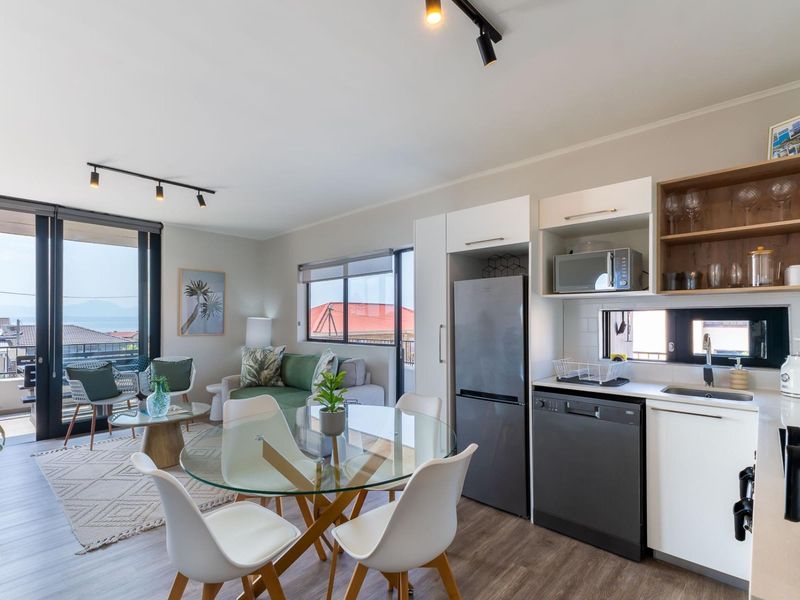 Modern open-plan living area featuring a contemporary kitchen with built-in cabinetry, track lighting, and seamless access to a private balcony with scenic views.