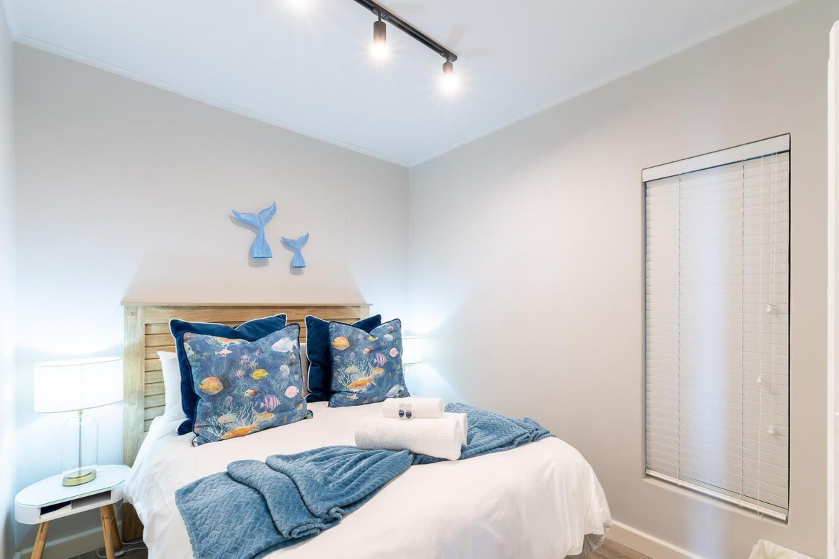 A well-maintained bedroom featuring neutral wall tones, modern track lighting, and fitted venetian blinds.