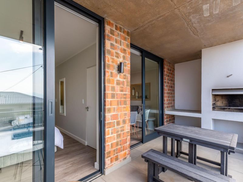 Covered balcony featuring a built-in braai, exposed brick accents, and concrete ceiling, providing seamless indoor-outdoor flow through large sliding glass doors.