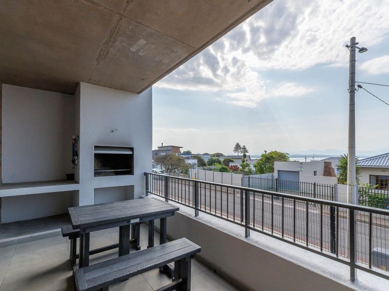 Covered balcony featuring a built-in braai, tiled flooring, and metal railings, offering an elevated outdoor space with neighbourhood views.