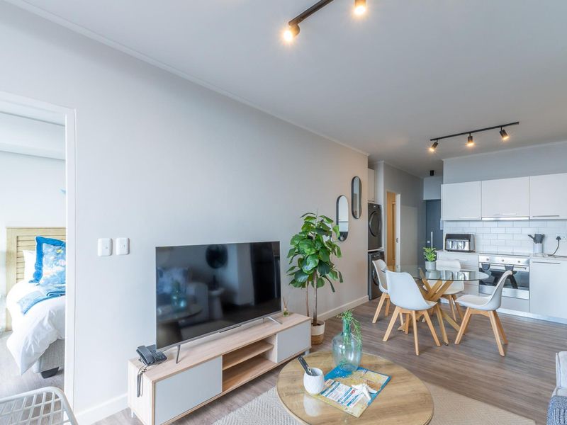 Modern open-plan living area featuring laminate flooring, track lighting, and a contemporary kitchen with built-in appliances and subway tile backsplash.