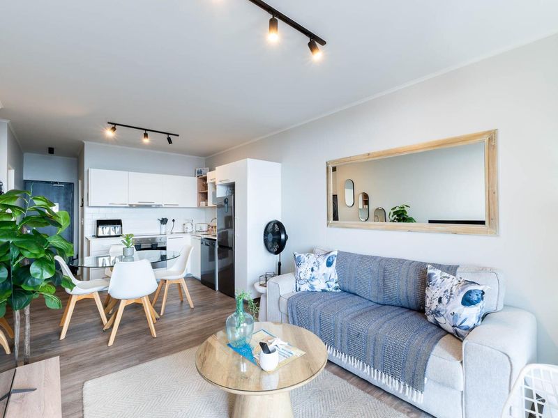 Modern open-plan living area featuring laminate flooring, track lighting, and a compact kitchen with built-in cabinetry and appliances.