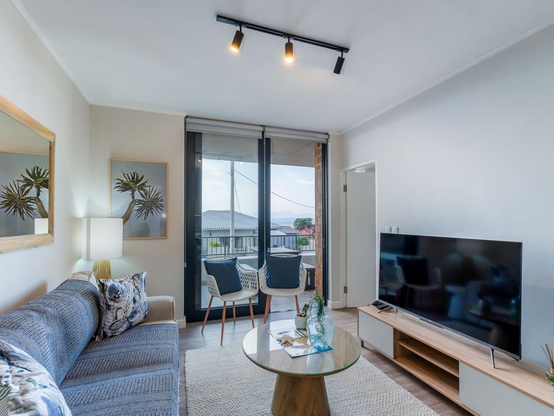 A well-lit living room featuring modern track lighting, laminate flooring, and a sliding glass door providing access to an outdoor balcony area.