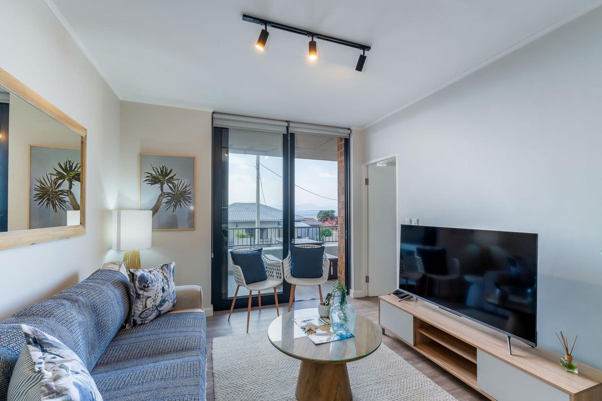 A well-lit living room featuring modern track lighting, laminate flooring, and a sliding glass door providing access to an outdoor balcony area.