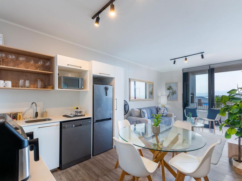 Modern open-plan living area featuring a compact kitchen with built-in cabinetry, track lighting, and seamless access to a private balcony.
