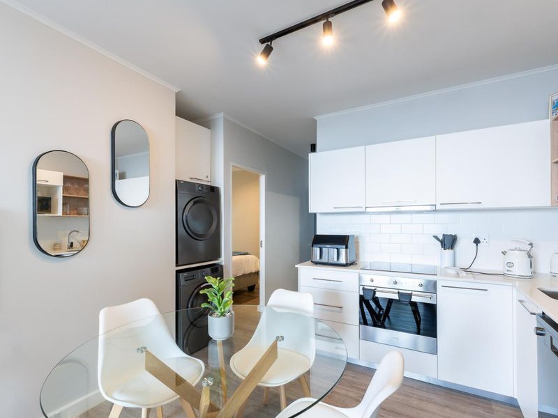 Modern open-plan kitchen featuring white cabinetry, subway tile backsplash, integrated appliances, and a convenient stacked laundry area.