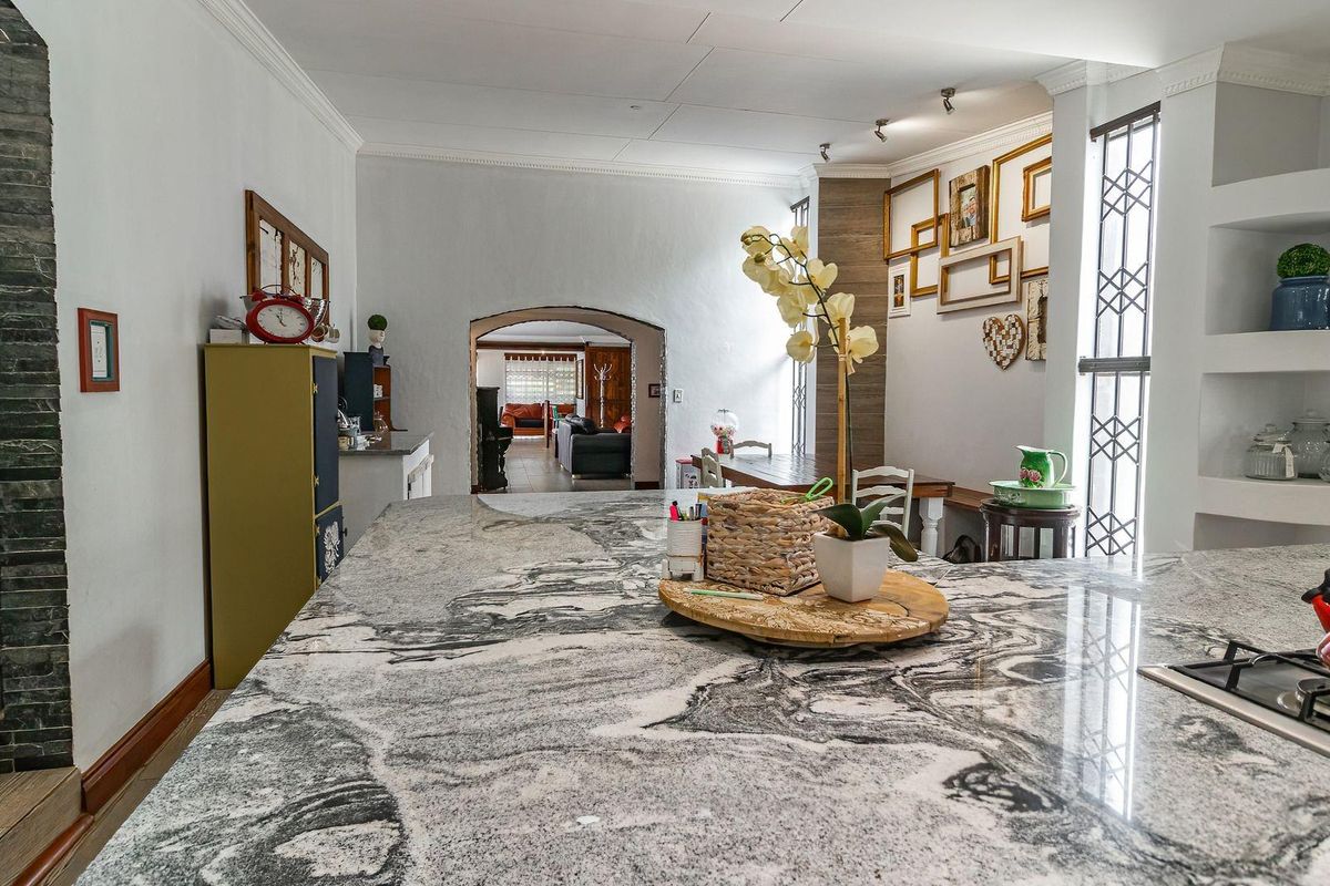 Spacious kitchen featuring a large granite island with an integrated gas hob, complemented by built-in shelving and an elegant arched entryway.