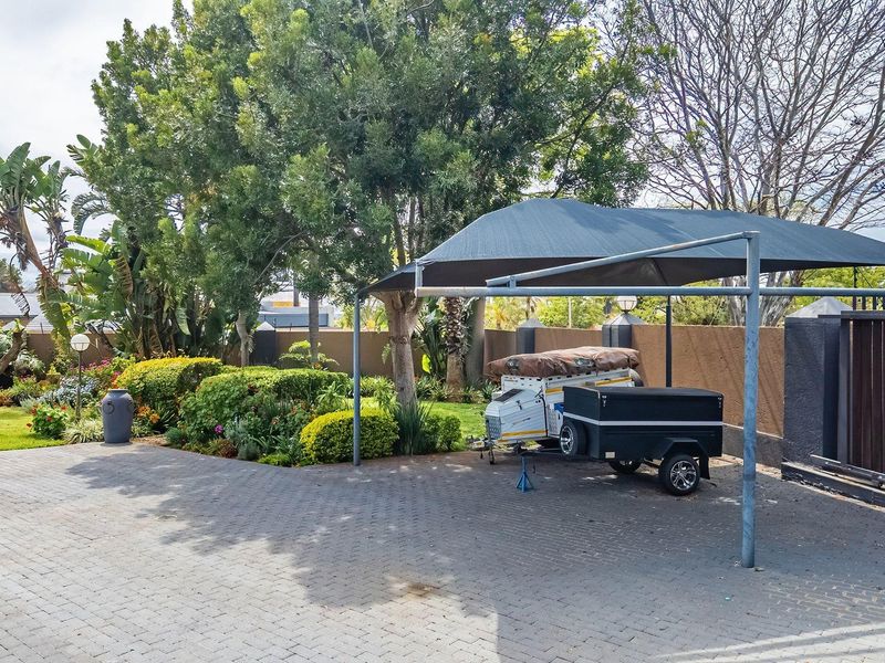 A paved front driveway featuring a shade cloth carport, secure sliding gate, and established garden landscaping.