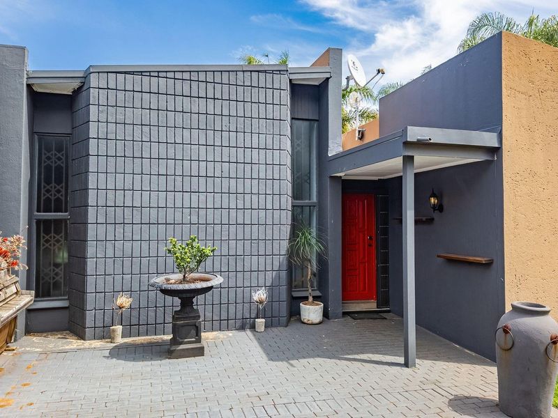 Front entrance area featuring a paved driveway, covered porch, and modern dark grey brick facade with a contrasting red front door.