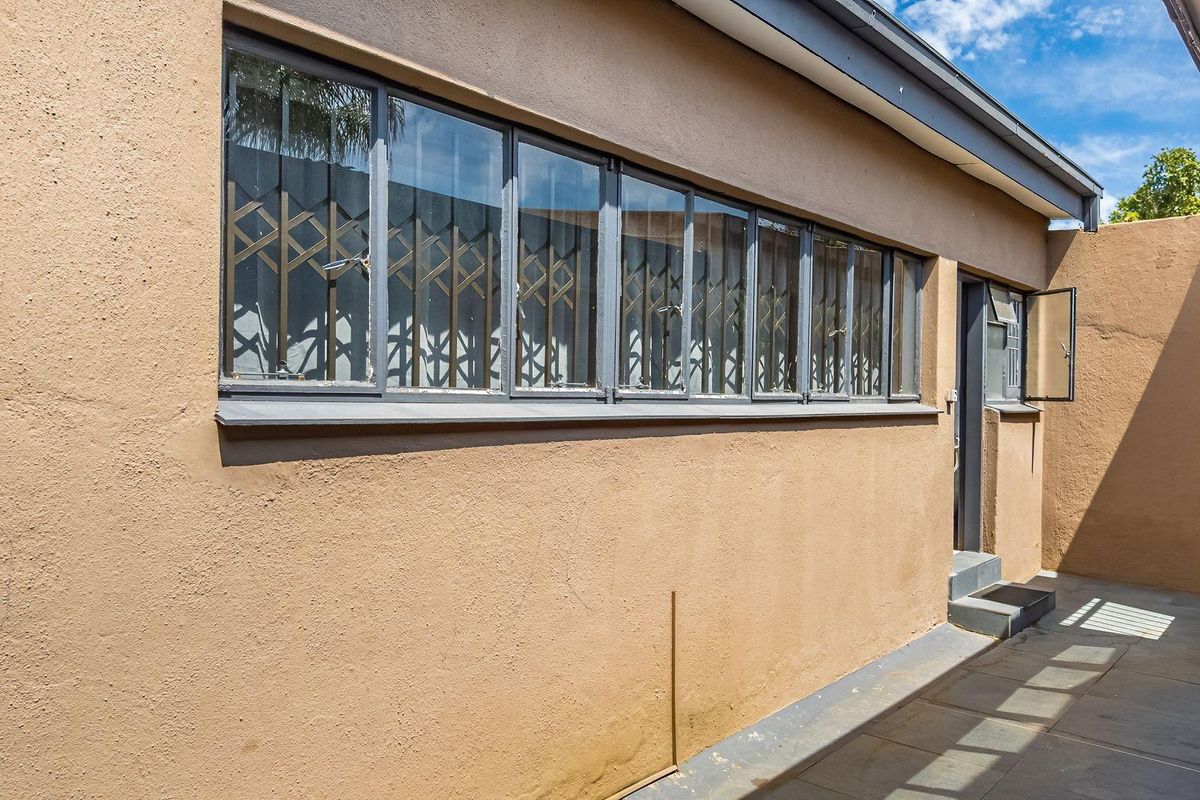 A view of the rear exterior wall featuring steel-framed windows with security gates and a paved walkway.