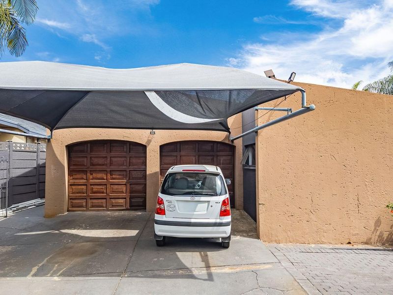 Front exterior view of the property featuring a double garage with wooden doors and a large shade sail covering the paved driveway area.