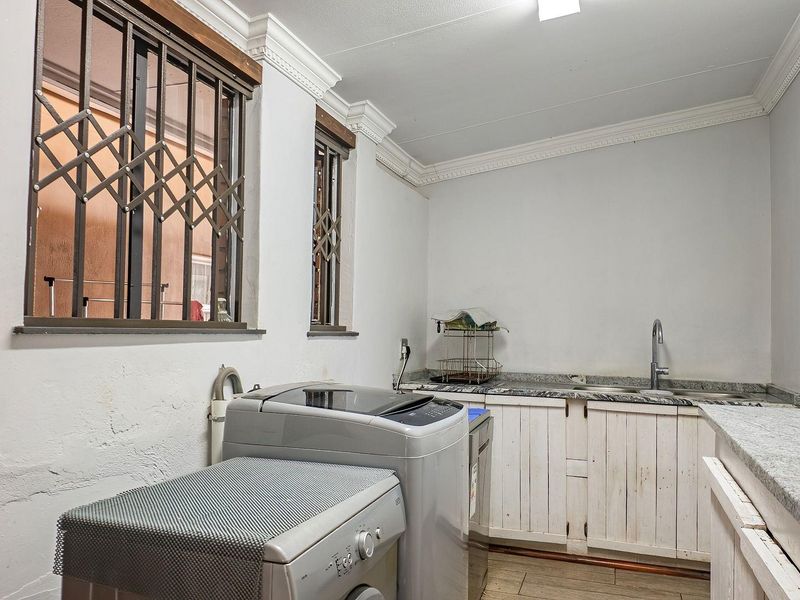 Functional laundry room featuring granite countertops, built-in cabinetry, and a stainless steel sink, with security bars on the windows.