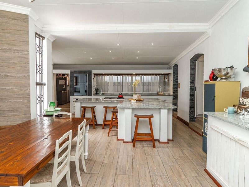 Spacious open-plan kitchen and dining area featuring a large central island with granite countertops, recessed lighting, and modern wood-look tile flooring.