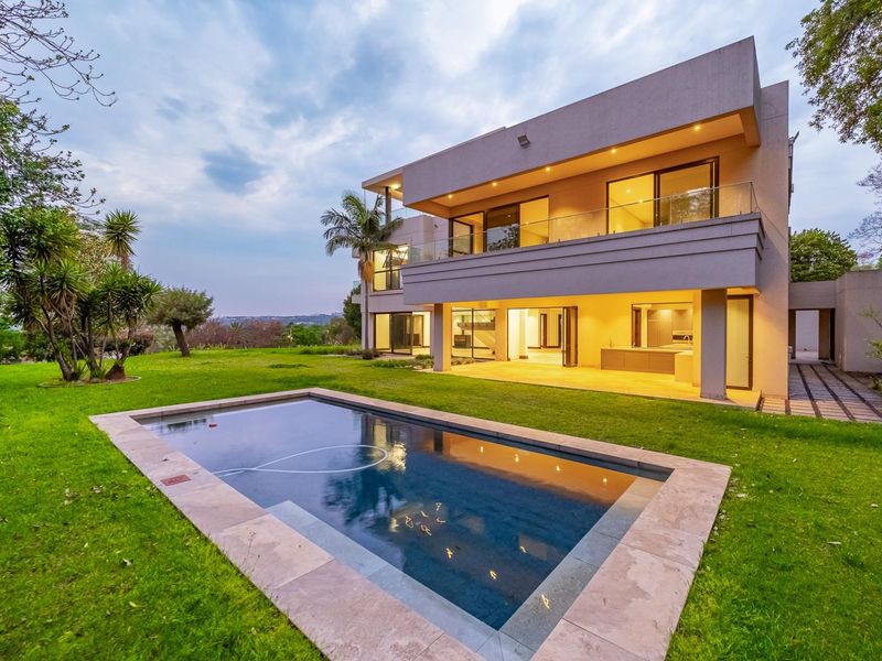 Modern double-story residence featuring a rear patio, glass balcony railings, and a swimming pool set within a spacious landscaped garden.