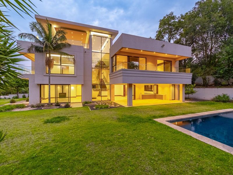 Modern multi-story residence featuring expansive glass facades, multiple balconies, a covered patio area, and a swimming pool set within a landscaped garden.