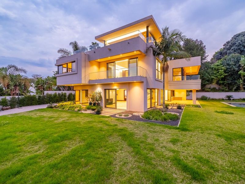 A modern multi-level luxury residence featuring expansive glass sliding doors, glass balustrades, integrated lighting, and a well-maintained garden with a swimming pool.