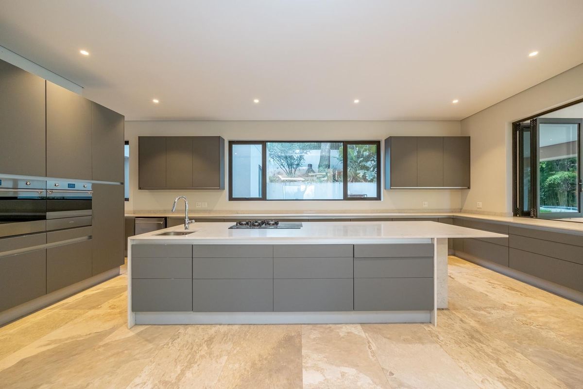 Modern, spacious kitchen featuring a large central island, stone countertops, handleless cabinetry, built-in oven, gas hob, and high-quality stone floor tiles.