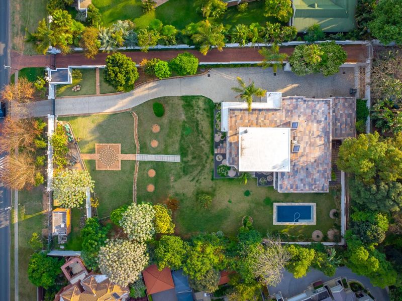 Aerial view of a residential property featuring a large landscaped garden, swimming pool, paved driveway, and a house with a tiled roof.
