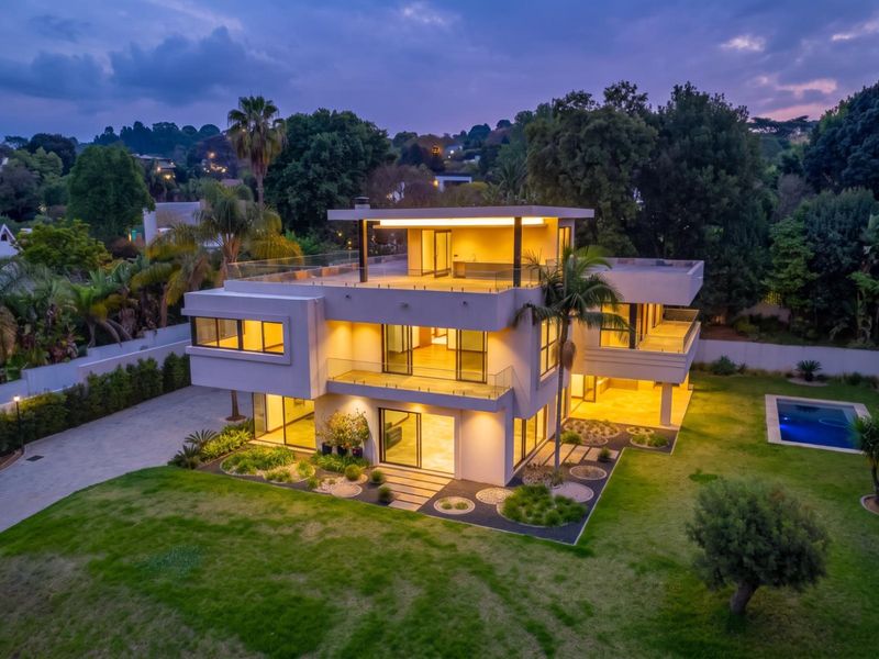 Stunning modern multi-level architectural home featuring expansive glass facades, multiple balconies, a swimming pool, and beautifully landscaped grounds at twilight.