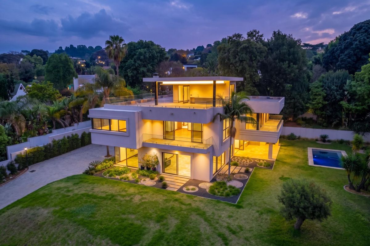 Stunning modern multi-level architectural home featuring expansive glass facades, multiple balconies, a swimming pool, and beautifully landscaped grounds at twilight.