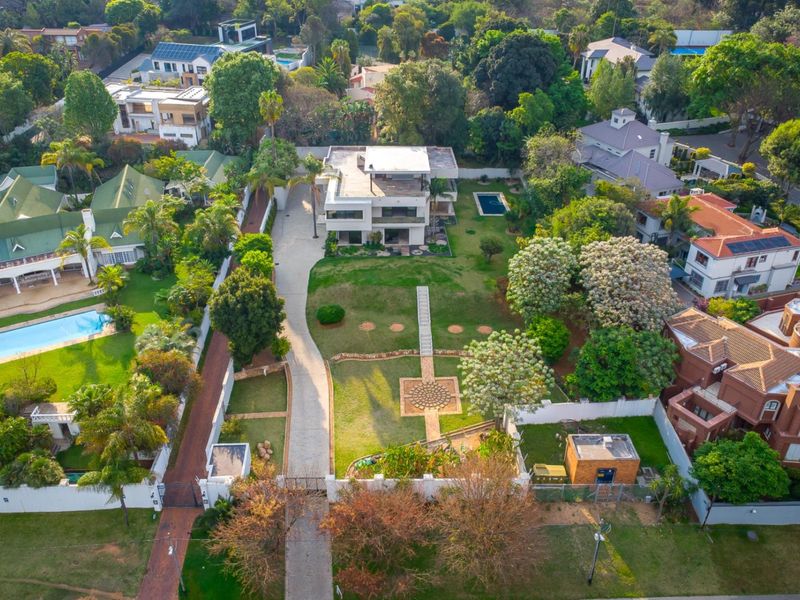 Aerial view of a large residential property featuring a multi-level home, expansive landscaped garden, paved driveway, and a private swimming pool.