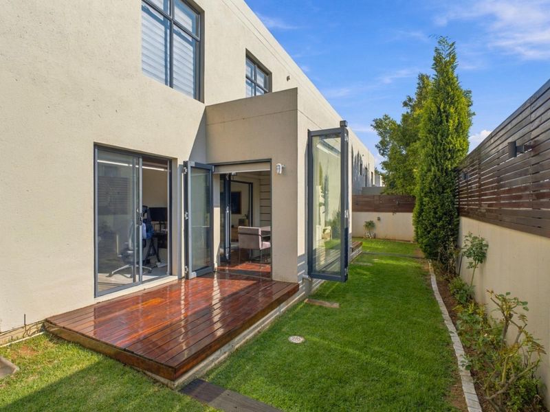 Rear view of the townhouse featuring a timber deck, bi-fold doors leading to the interior, and a well-maintained private garden with timber fencing.