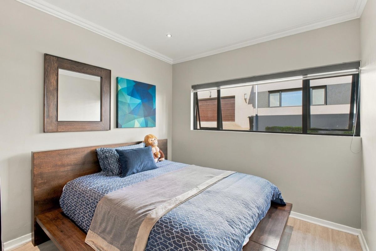 A well-maintained bedroom featuring neutral wall tones, recessed downlighting, decorative cornice, and a large window with a fitted roller blind.