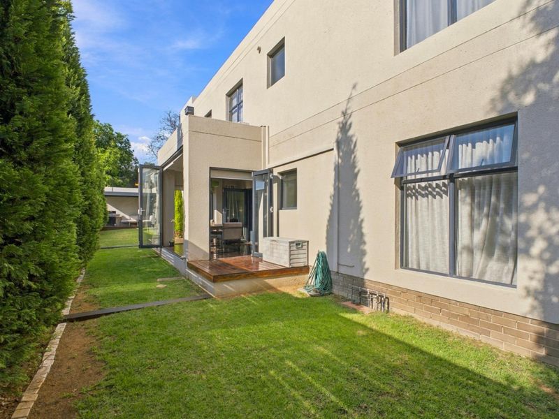 Rear view of the townhouse featuring a well-maintained garden, timber decking, and modern bi-fold doors providing seamless indoor-outdoor flow.