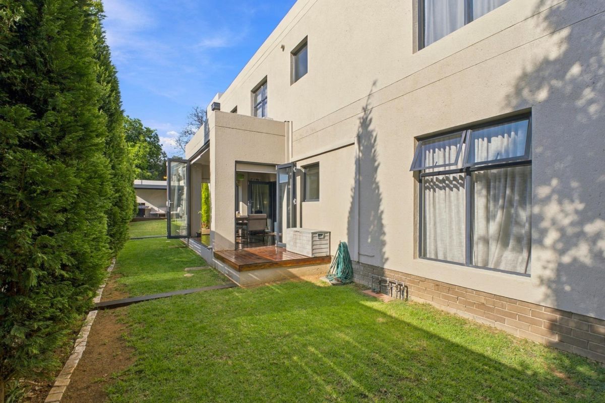 Rear view of the townhouse featuring a well-maintained garden, timber decking, and modern bi-fold doors providing seamless indoor-outdoor flow.