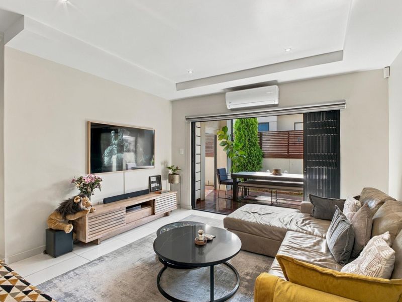 Modern living room featuring recessed ceilings, downlights, and a split-system air conditioner, with seamless access to an outdoor patio through large sliding glass doors.