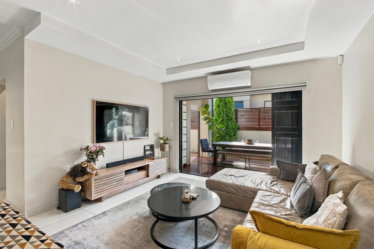 Modern living room featuring recessed ceilings, downlights, and a split-system air conditioner, with seamless access to an outdoor patio through large sliding glass doors.