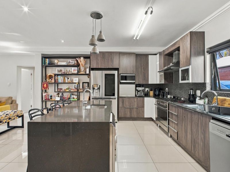 Modern open-plan kitchen featuring dark wood cabinetry, stone countertops, a central island, and high-quality built-in appliances, seamlessly flowing into the living area.