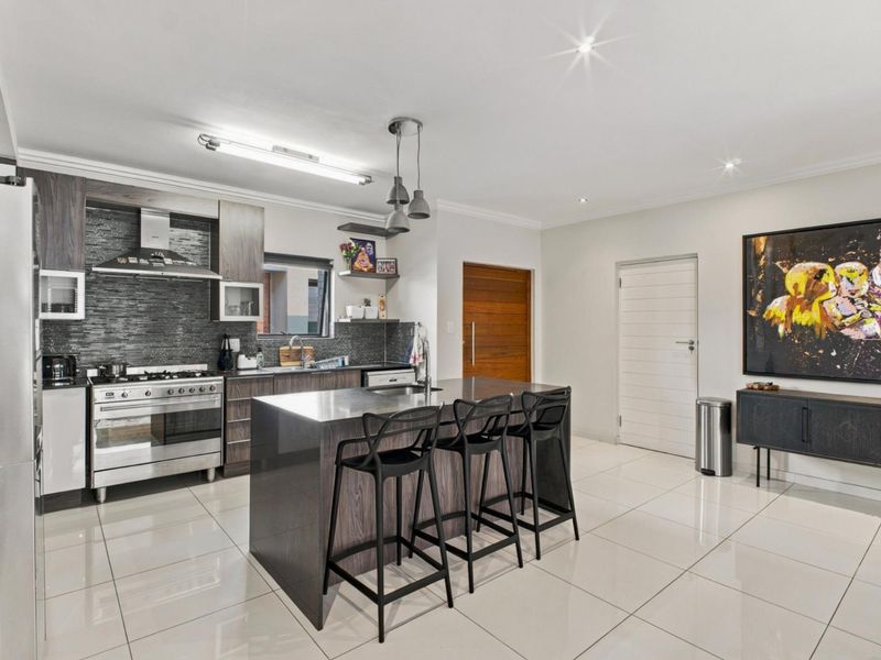Modern kitchen featuring a central island, gas stove, extractor fan, sleek cabinetry, and polished tiled flooring, offering a functional and contemporary cooking space.