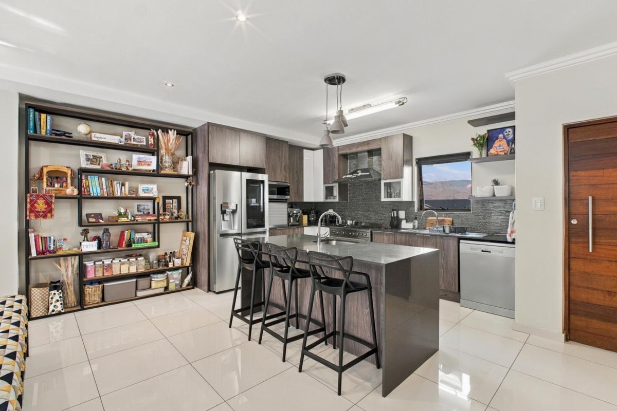 Modern kitchen featuring dark wood cabinetry, stone countertops, a central island with seating, and high-quality built-in appliances with polished tile flooring.