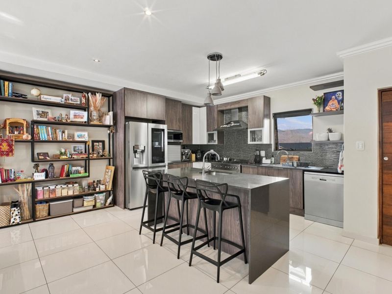 Modern kitchen featuring dark wood cabinetry, stone countertops, a central island with seating, and high-quality built-in appliances with polished tile flooring.