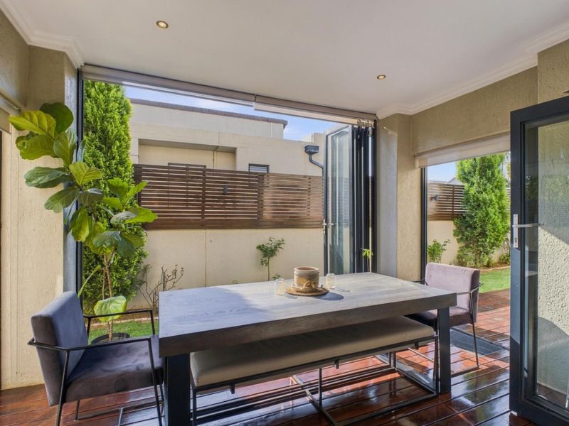 A modern covered patio featuring timber decking, recessed lighting, and bi-fold doors that open to a private garden area with timber slat fencing.