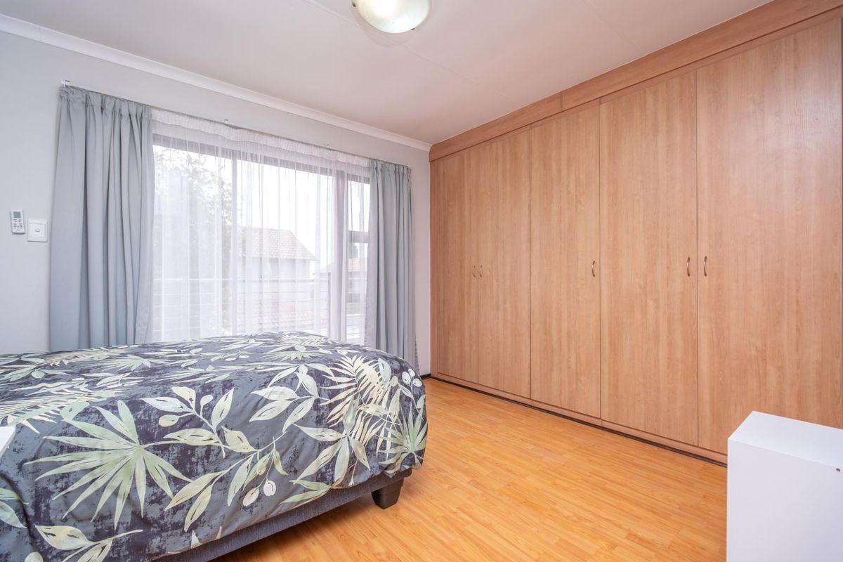 A well-maintained bedroom featuring extensive floor-to-ceiling built-in wooden cupboards and durable laminate flooring, offering ample storage space.
